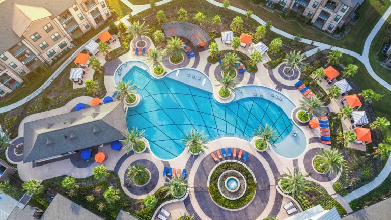 Hollyhock Street: A gorgeous commercial outdoor pool that features a volleyball net, decorative floor tiles, a raised fountain, raised planters, entry seats, and knee walls.